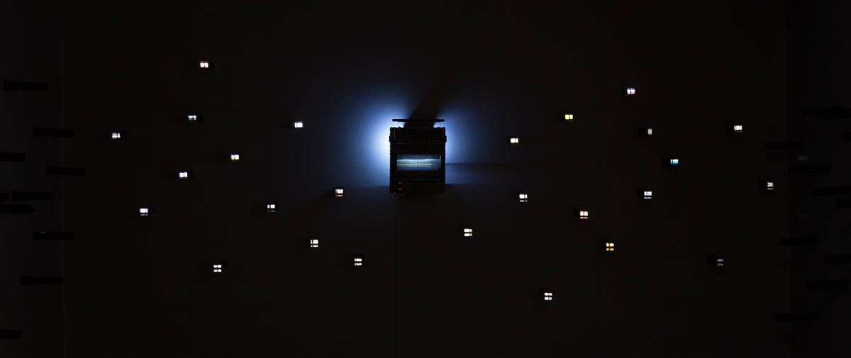 work by Arya Tabandehpoor, series of small luminous cubes around a luminous machine for viewing photos