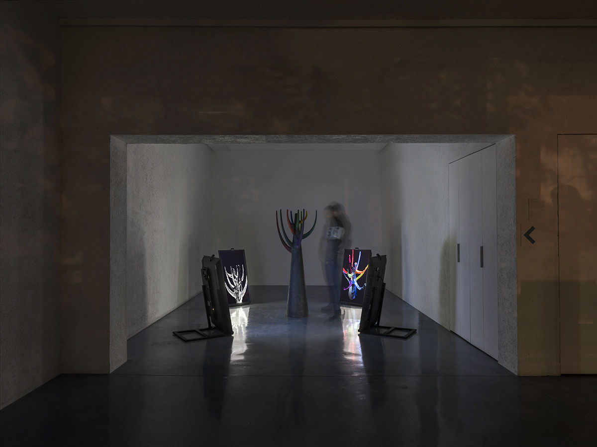 vue de l'installation, sculpture au centre du salle noire, elle représente une sorte d'arbre géométrique, autour quatre écrans projetent des images 3D de la sculpture et réagissent à la présence du public